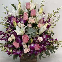 Pink roses and white lilies in a wooden box with purple orchids