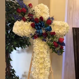 Cross-shaped floral tribute with white flowers, red roses, and a blue ribbon