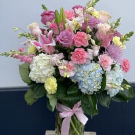 Mixed pastel bouquet in a glass vase with pink, blue, and white blooms