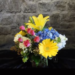 Mixed bouquet in a glass vase with yellow lilies, blue hydrangea, pink roses, and white blooms
