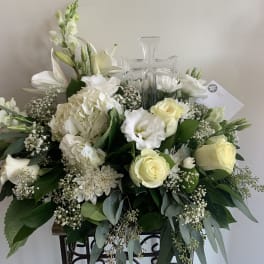 White floral arrangement with roses, lilies, and a clear glass cross