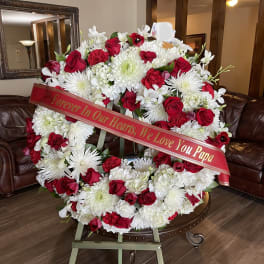 Large red and white funeral wreath on an easel with a memorial ribbon