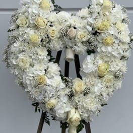 Heart-shaped white floral wreath with cream roses on a stand