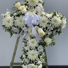 White floral cross wreath with a ribbon bow on an easel