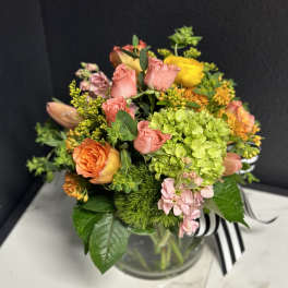 Mixed bouquet of pink, orange, yellow, and green flowers in a glass vase