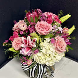 Pink and white floral arrangement in a round vase with a striped ribbon