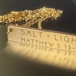Gold necklace with a rectangular pendant engraved "SALT + LIGHT"