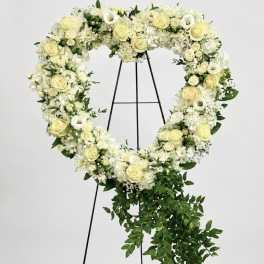 Heart-shaped floral wreath of white and pale yellow flowers on a black stand