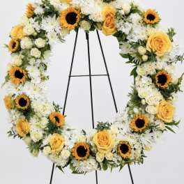 Heart-shaped floral wreath with yellow roses, white flowers, and sunflowers on an easel