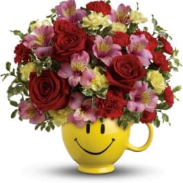 Bouquet of red roses and pink flowers in a yellow smiley-face mug