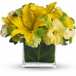 Yellow lilies and green-white flowers arranged in a square glass vase