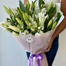 Bouquet of white lilies and small white daisies wrapped in pale pink paper