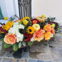 Low floral centerpiece with orange roses, sunflowers, and white blooms in a wooden box