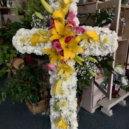 Cross-shaped floral tribute with white blooms, yellow lilies, and pink roses