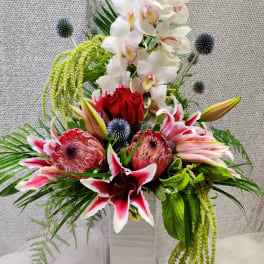 Tall floral arrangement with white orchids, red roses, and pink lilies in a white vase