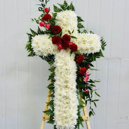 White floral cross on a wooden easel with red carnations