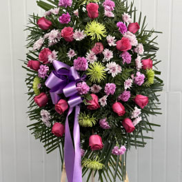 Standing floral wreath with pink roses, chrysanthemums, and a purple ribbon