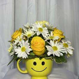 Yellow smiley-face mug filled with yellow roses and white daisies