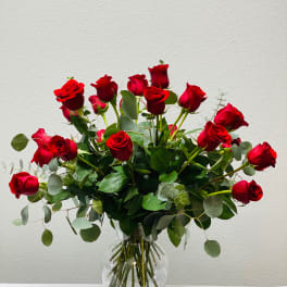 Red roses arranged in a clear glass vase with eucalyptus foliage