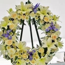 Floral wreath with pale lilies, cream roses, and purple accents on a black stand
