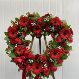 Heart-shaped red flower wreath on a wooden stand with ribbon