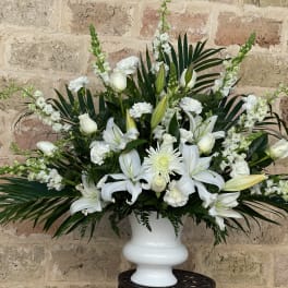 White lilies and roses arranged in a white urn vase