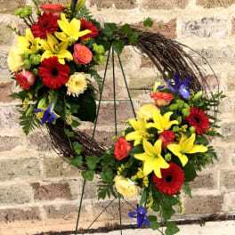 Circular floral wreath with red, yellow, and pink blooms on a metal stand