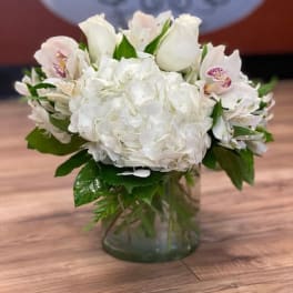 White hydrangea and pale pink orchid arrangement in a glass vase