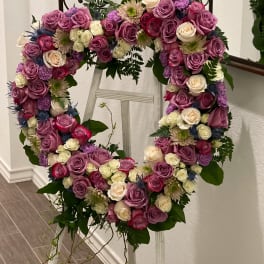 Heart-shaped floral wreath of pink, purple, and white roses on a stand
