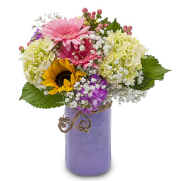 Mixed bouquet with pink gerberas, sunflowers, hydrangeas, and a purple vase