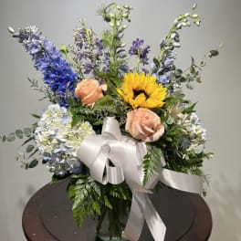 Mixed bouquet with sunflowers, roses, and blue flowers in a glass vase