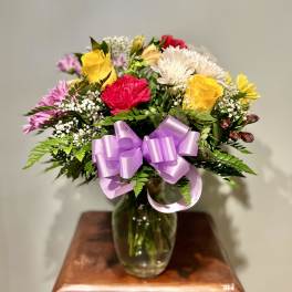 Mixed bouquet of roses and daisies in a glass vase with a lavender ribbon