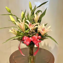 Pink lilies in a clear glass vase with a bright ribbon bow