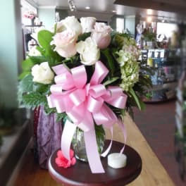 Pink and white rose bouquet in a glass vase with a large pink ribbon