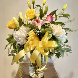 Bouquet of yellow roses, lilies, and white hydrangeas in a glass vase