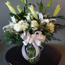 White lilies and roses arranged in a glass vase with a white ribbon