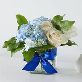 Blue hydrangeas and white roses in a glass vase with a blue ribbon