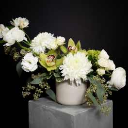 White floral arrangement in a beige vase with green orchids and roses
