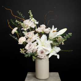 White lilies and pale roses in a tall vase with curly branches