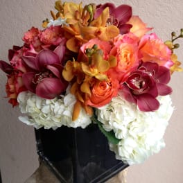 Bouquet of orchids, roses, and white hydrangeas in a black vase