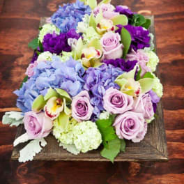 Bouquet of lavender roses, blue hydrangeas, and orchids on a wooden tray