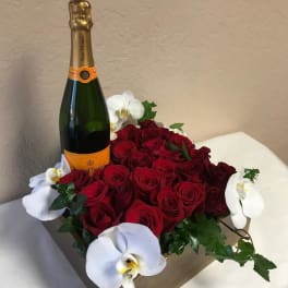 Red roses arranged with white orchids and a champagne bottle