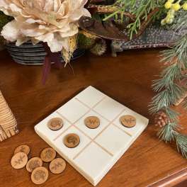 Tic-tac-toe board with wooden game pieces on a table beside a floral arrangement