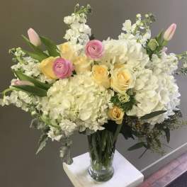 Bouquet of white hydrangeas, yellow roses, and pink tulips in a glass vase