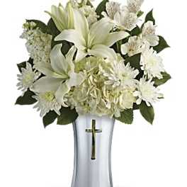 White floral arrangement in a silver vase with a cross emblem