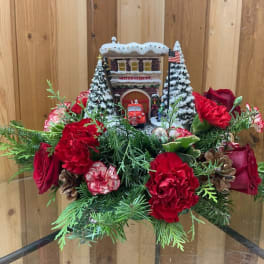 Christmas floral arrangement with red roses and carnations around a small snowy building
