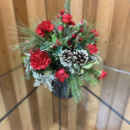 Holiday arrangement with red carnations, pinecones, and evergreen in a black container