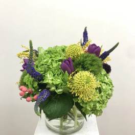 Mixed bouquet in a clear glass vase with green hydrangeas and purple blooms
