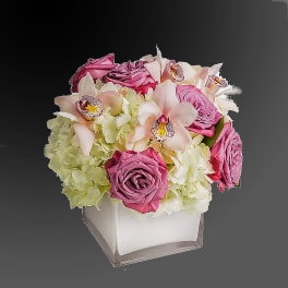 Pink roses and pale orchids arranged in a white square vase