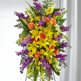 Tall standing floral spray with yellow lilies, orange roses, and purple flowers